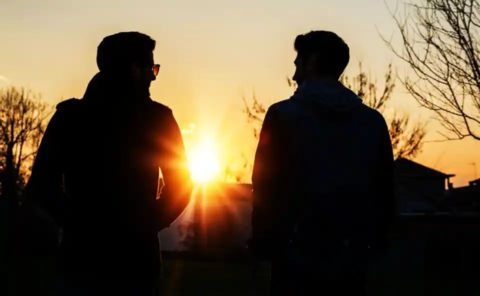 silhouette of two men sitting outside talking at sunset